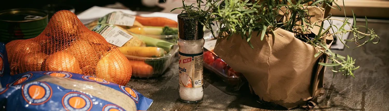 Ein Netz Zwiebeln, ein Salzstreuer und ein Thymiantopf stehen auf einem Holztisch.