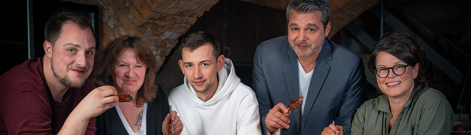 Drei Männer und zwei Frauen mit unterschiedlich farbiger KLeidung schauen in die Kamera und lachen.