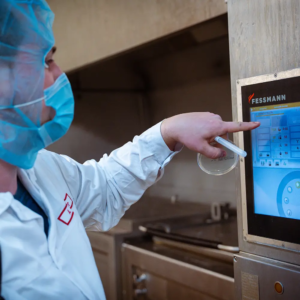 Hygiene und Technik vereint: Mitarbeiter in Schutzkleidung steuert präzise Produktionsprozesse in der Lebensmittelverarbeitung über modernes Touchscreen-System.