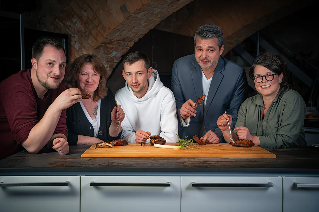 Fünf Personen des Metzgerei Lindörfer Teams sitzen an einem Küchentresen und essen Fleisch. Von links nach rechts: André Mayer (Qualitätsmanagement), Bettina Marx (Vertriebsinnendienst), ein junger Mann ohne Namensnennung, Christian Kohlschütter (Leiter Verwaltung) und Jacqueline Kohlschütter (Geschäftsführung).