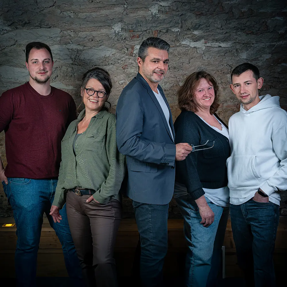 Ein Mann im weinroten Pullover, eine Frau in dunkelgrüner Bluse, ein Mann im blauen Sakko, eine Frau in schwarzer Strickjacke und ein Mann im weißen Kapuzenpullover stehen eng neben einander und lächeln in die Kamera.